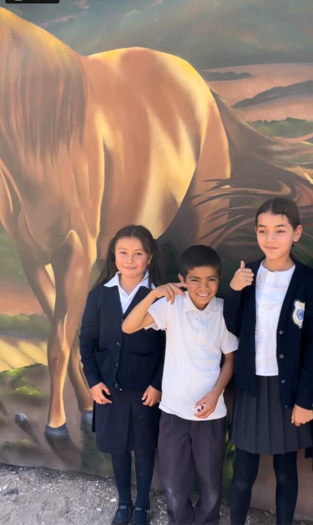 Three children posing for a picture in front of a horse mural.