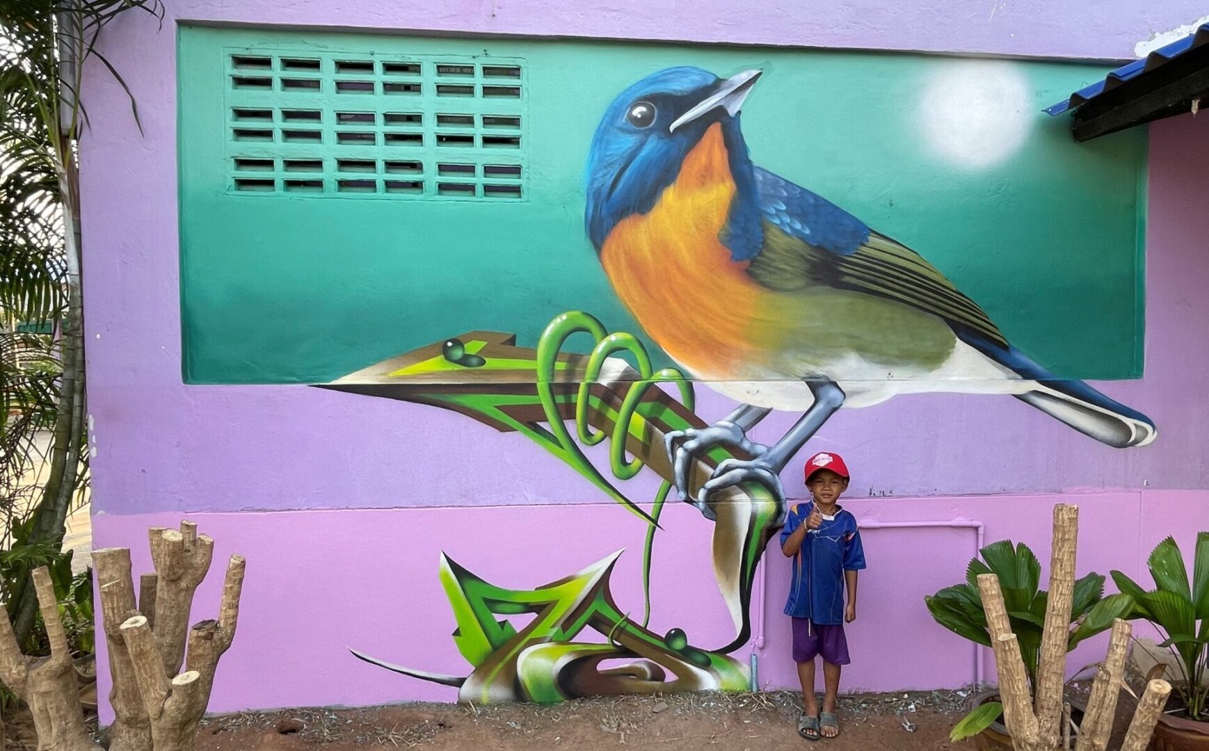 A boy standing in front of a mural with a bird on it.