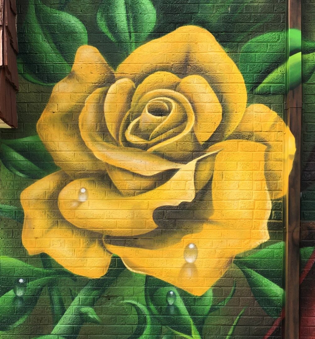 A painting of a yellow rose on the side of a building.