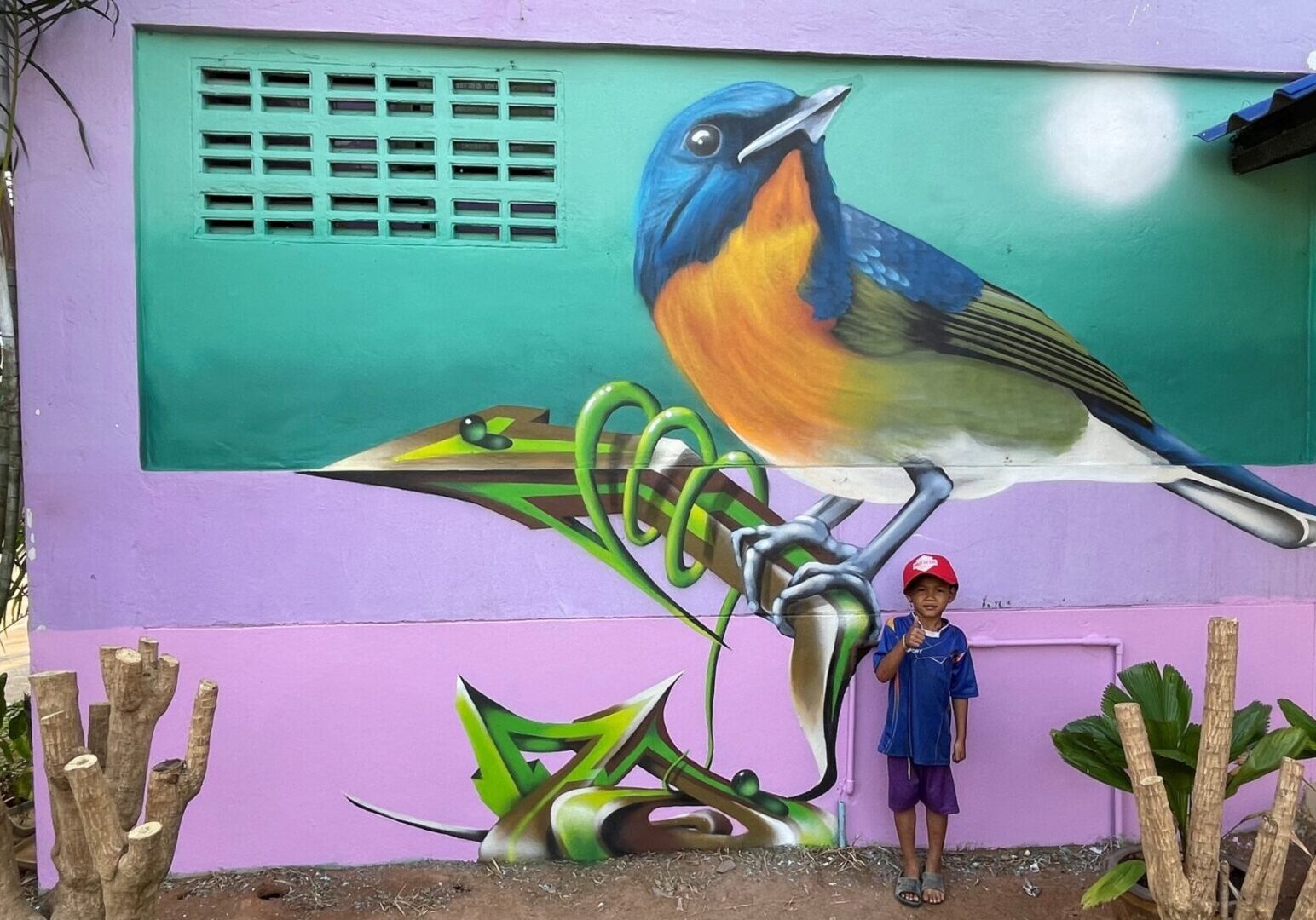 A boy standing in front of a mural with a bird on it.